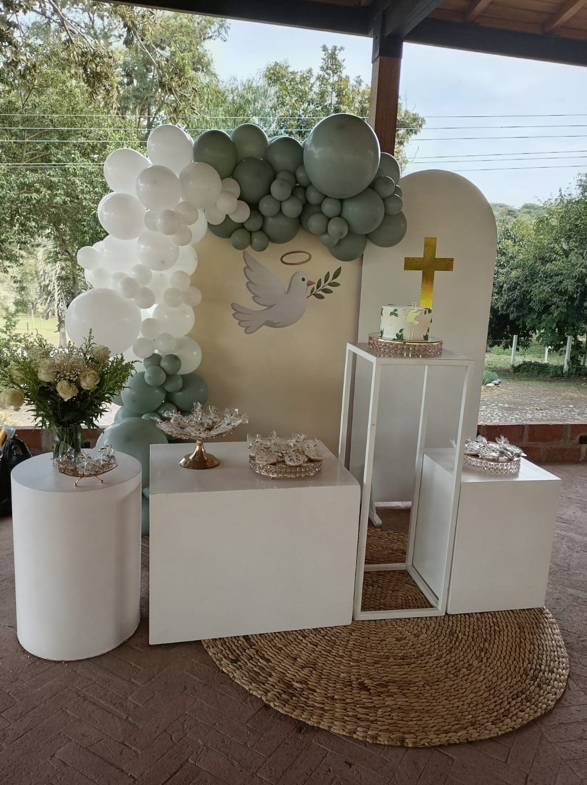 Decoración de bautizo con globos verdes y blancos, paloma y cruz dorada