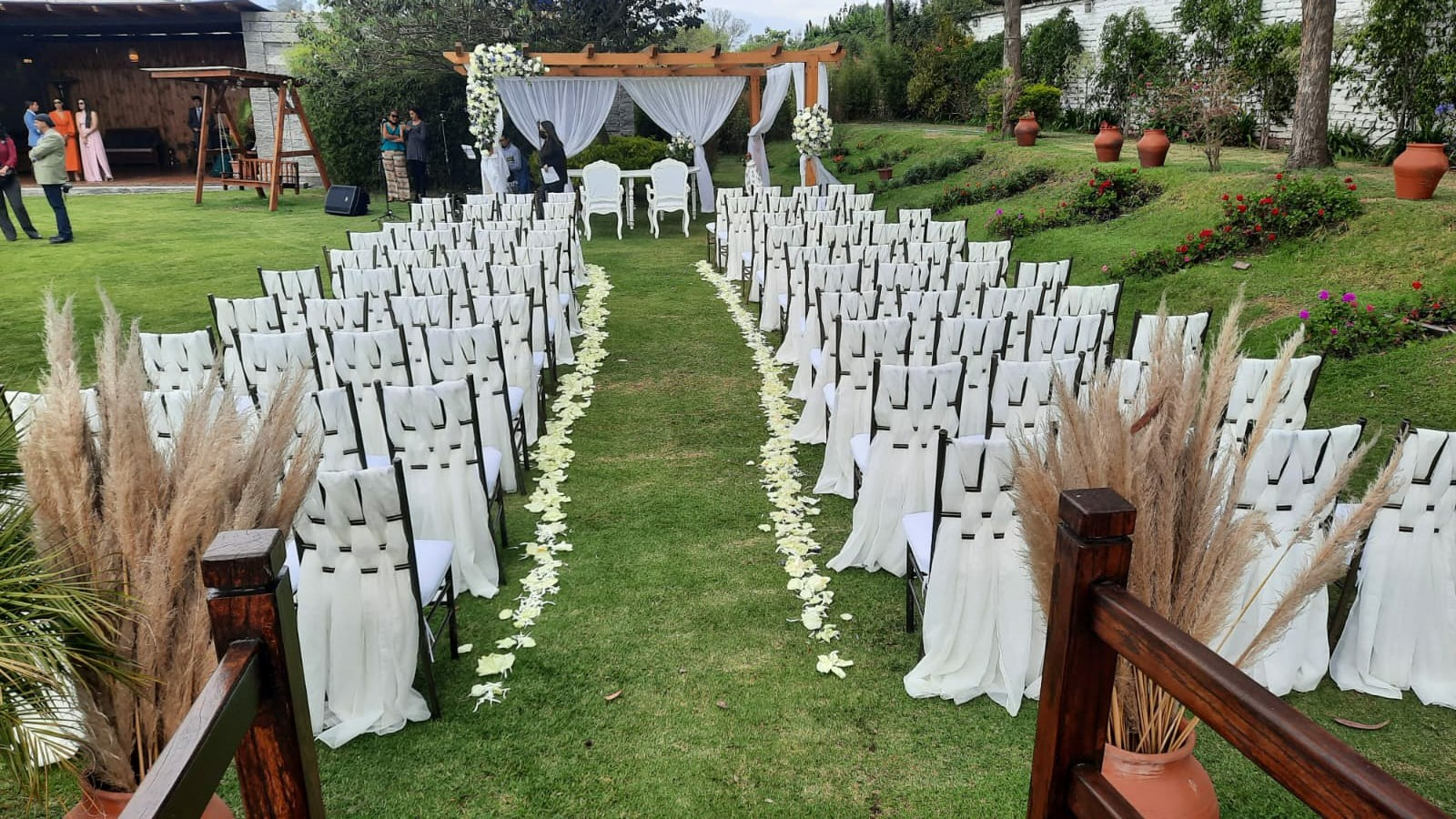 Ceremonia de boda al aire libre con sillas blancas y pétalos
