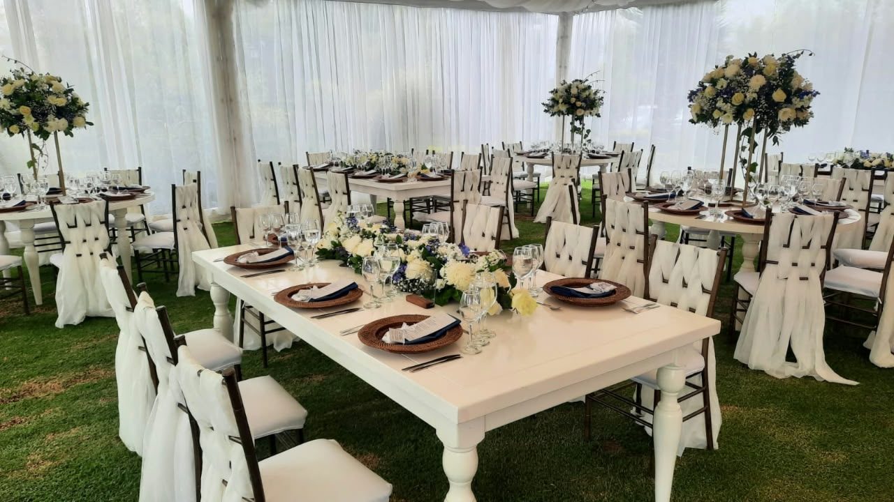 Mesas de banquete blancas con arreglos florales bajo carpa para evento